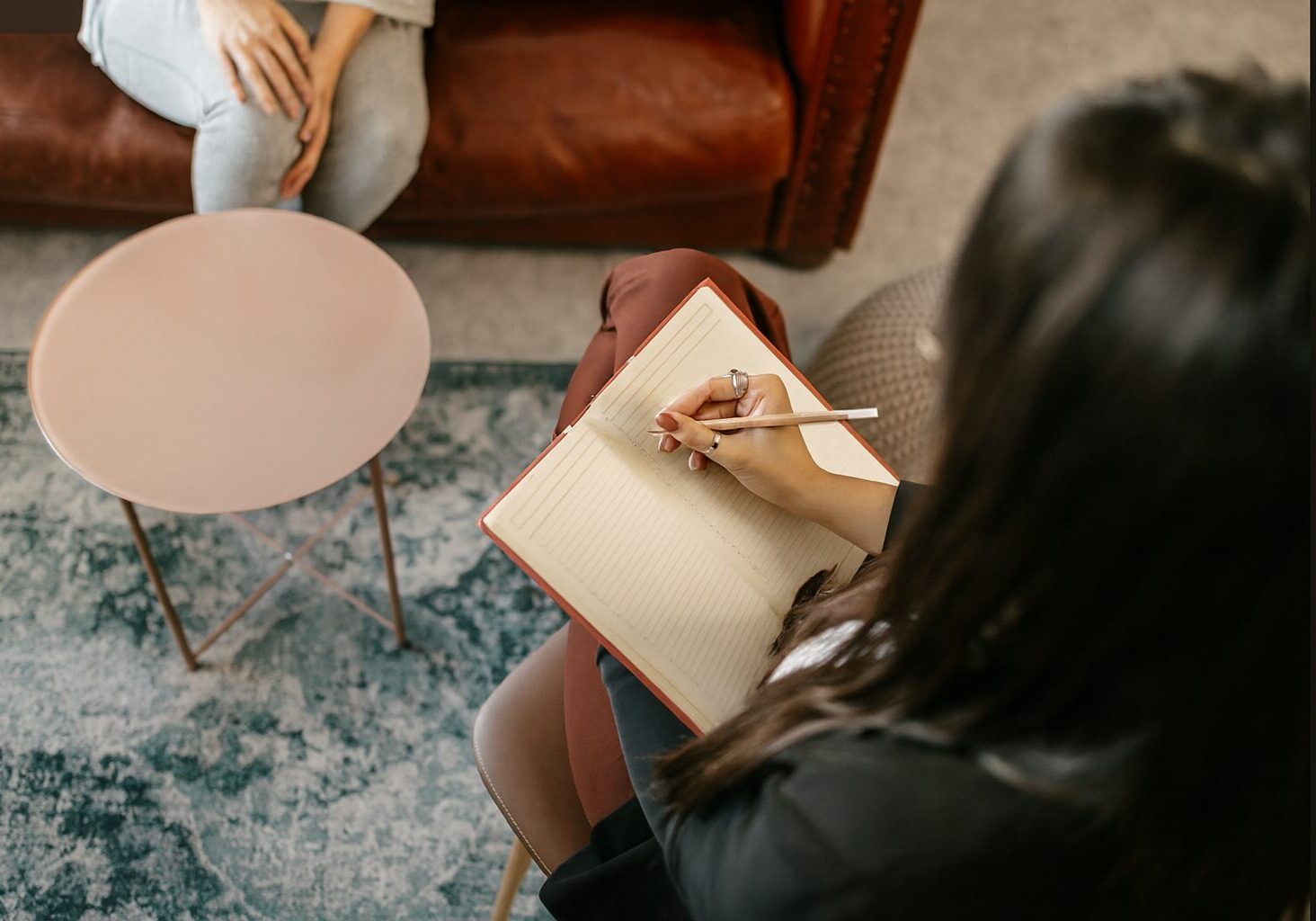 Person writing in a notebook while seated on a carpet.
